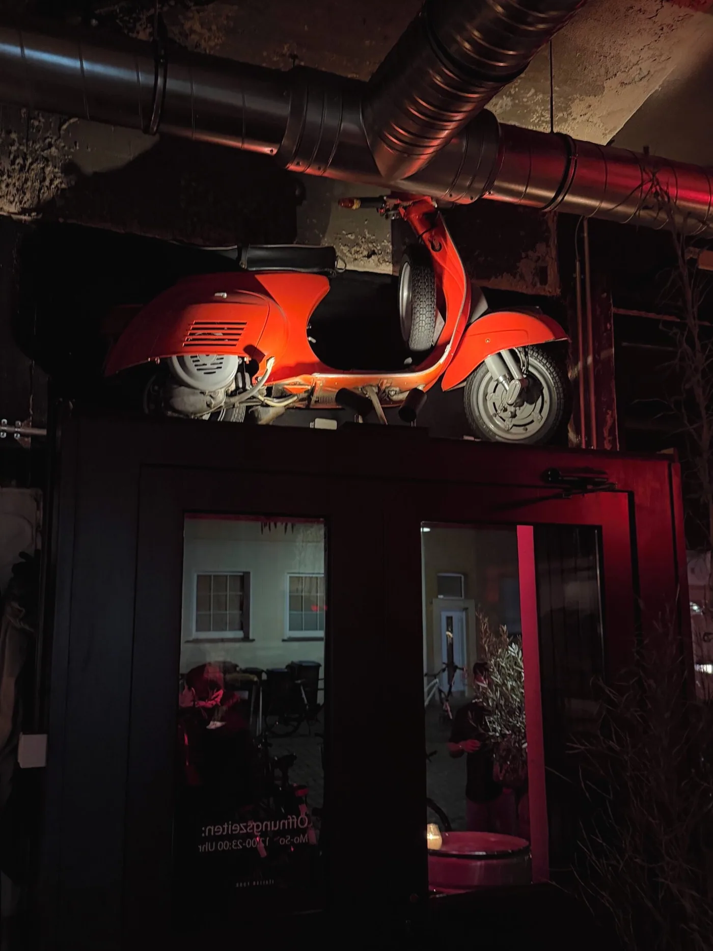 Eingang des Baci Baci am Abend mit roter Vespa über der Tür